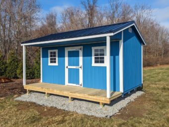 One of our blue and white Cape Cod Sheds For Sale in Lincoln Village OH - Bright blue siding with white framed windows and door-black overhanging roof supported by a white wooden post on each side from natural wood porch