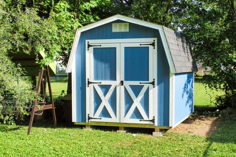 One of our Classic blue Sheds For Sale Lincoln Village OH - Blue siding with white trimmed double doors under white vent and gray roof - set on green grass amid trees