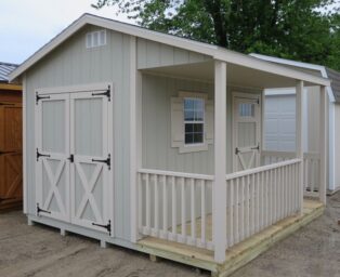 One of our gray and white cabin sheds in Urbana OH - Gray siding with white-trimmed double doors with matching fenced wood porch - Single white-trimmed entrance next to white-framed window beneath overhanging roof