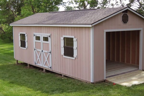 One of our Gable garage sheds in Urbana OH - Peach wood siding with white trimmed corners and double doors with windows and X detail - two windows with white shutters - open overhead door beneath octagonal window - Brown shingled gable style roof