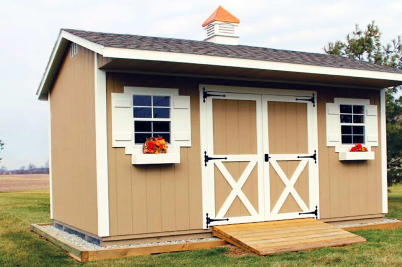 One of our beige quaker sheds in Urbana OH - beige siding with white-trimmed double doors between two windows with white shutters and window boxes - dark shingled roof with white and copper colored cupola