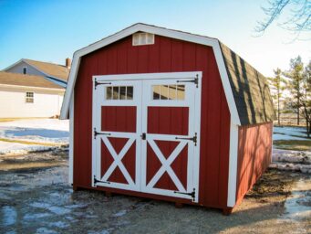 One of our classic red barn style sheds in Urbana OH - Red wood siding with white trimmed corners and double doors beneath white vent and black shingled roof
