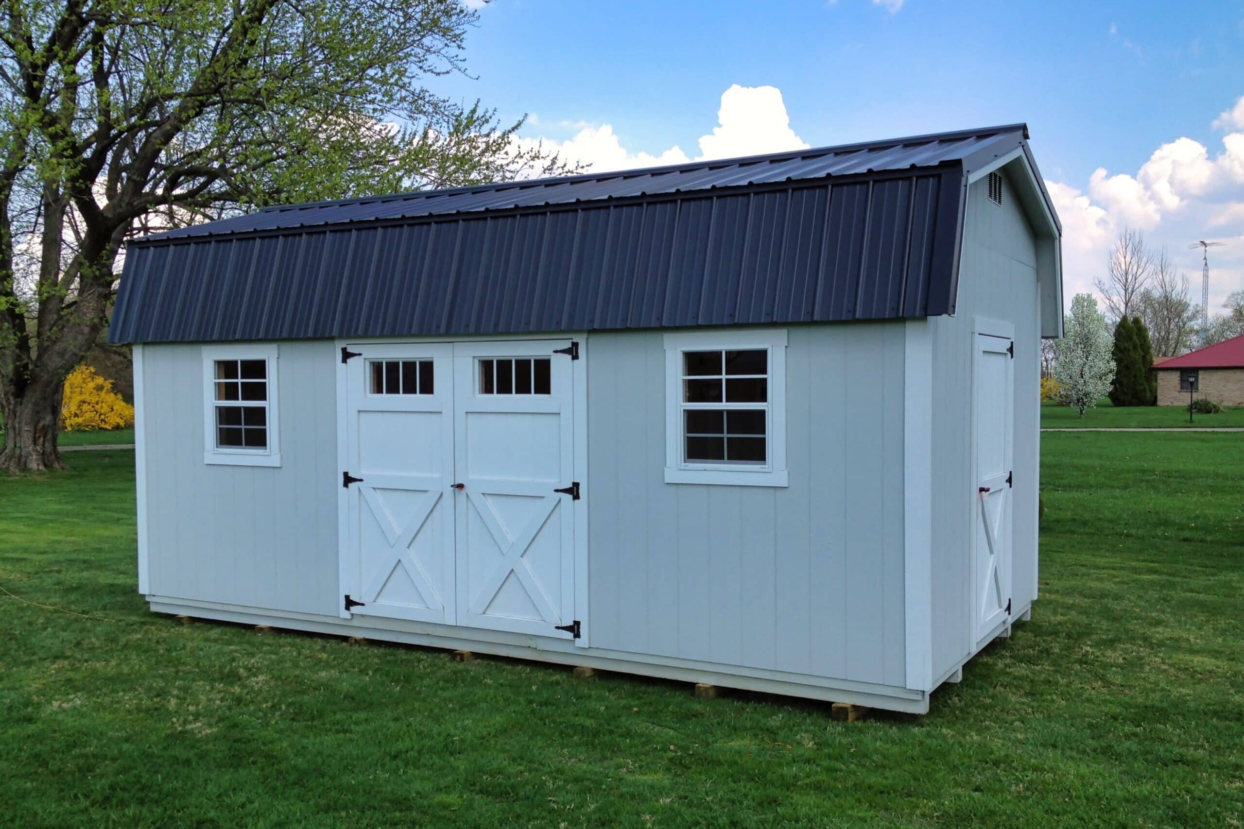One of our Highwall gray storage sheds for sale in Worthington OH - Light gray siding with white single and double doors and whiite trimmed windows beneath black roof - set on grassy lawn beside tree