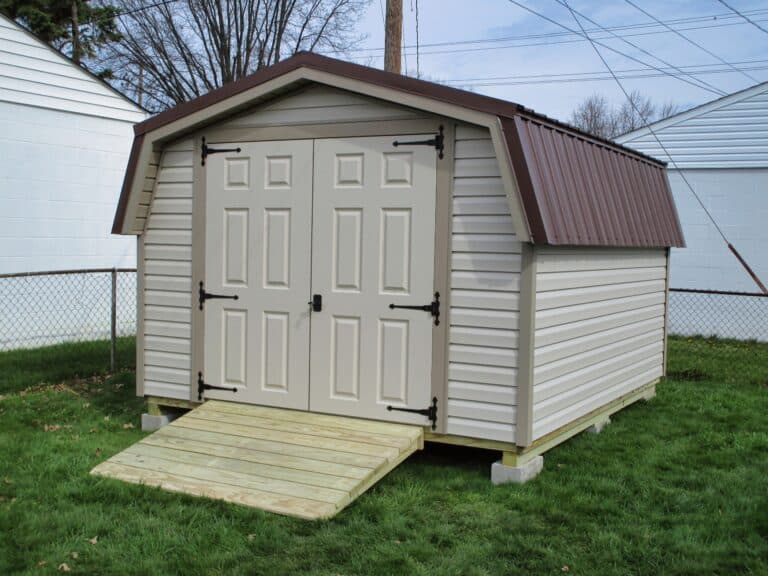 One of our beige and white mini barns sheds for sale in Worthington OH - Light beige siding with white double doors and brown roof - set on green lawn with natural wood ramp
